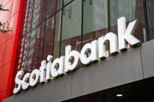 Logotipo iluminado de Scotiabank sobre una fachada de vidrio y paneles rojos, en un edificio contemporáneo de oficinas.
