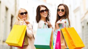 Tres mujeres sonrientes con bolsas de compra de colores, simbolizando el crecimiento del consumo planificado durante las promociones de Elektra.