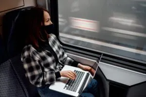 Profesional con laptop viajando en tren o aeropuerto simbolizando vivir y trabajar en diferentes ciudades.