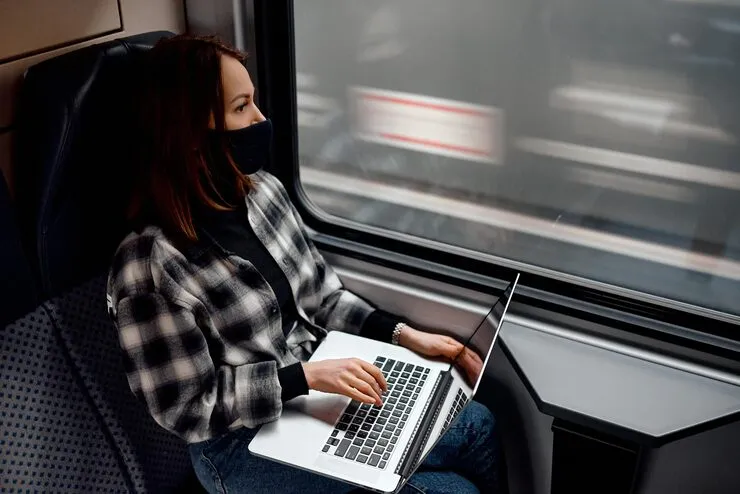 Profesional con laptop viajando en tren o aeropuerto simbolizando vivir y trabajar en diferentes ciudades.
